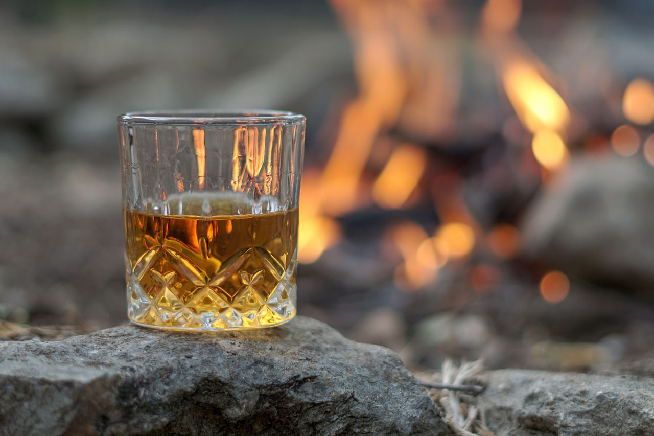 Glass of bourbon beside a fire